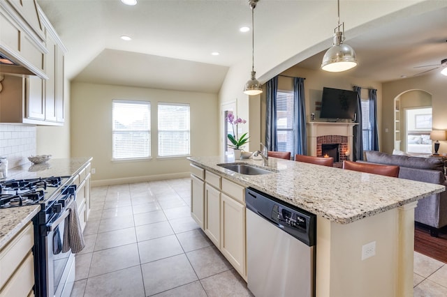 kitchen with pendant lighting, sink, appliances with stainless steel finishes, a center island with sink, and a brick fireplace