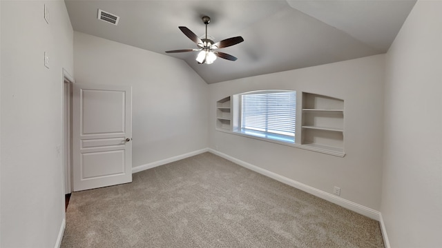 carpeted empty room with built in shelves, ceiling fan, and vaulted ceiling