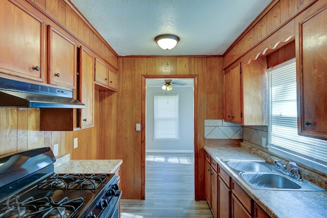 kitchen with sink, light wood-type flooring, ornamental molding, a textured ceiling, and black range with gas cooktop