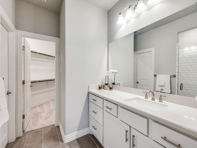 full bath with a walk in closet, a stall shower, vanity, baseboards, and tile patterned floors