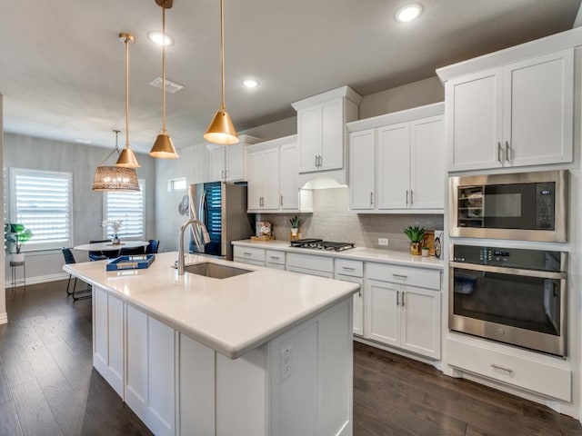 kitchen featuring appliances with stainless steel finishes, dark hardwood / wood-style floors, pendant lighting, a kitchen island with sink, and white cabinets