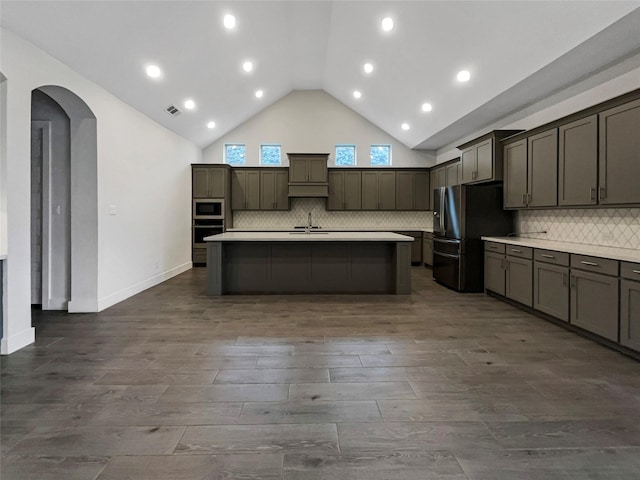 kitchen featuring sink, stainless steel appliances, dark hardwood / wood-style floors, high vaulted ceiling, and a center island with sink