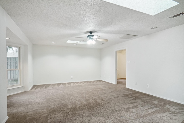 empty room with a textured ceiling, a skylight, ceiling fan, and carpet flooring