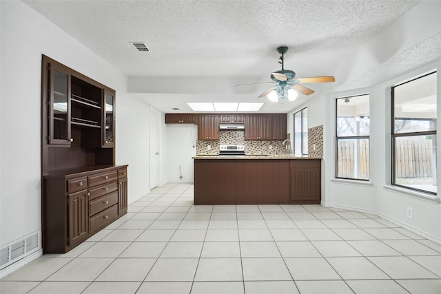 kitchen featuring a skylight, backsplash, light tile patterned floors, dark brown cabinetry, and kitchen peninsula