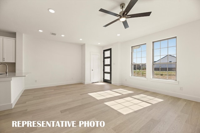 unfurnished living room with sink, light hardwood / wood-style floors, and ceiling fan