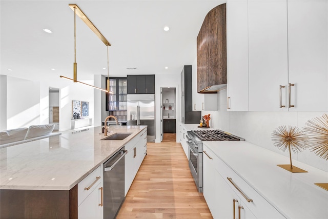 kitchen featuring sink, high quality appliances, light stone countertops, white cabinets, and a center island with sink