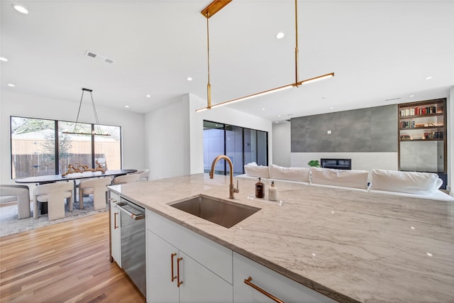 kitchen with sink, light stone counters, dishwasher, pendant lighting, and white cabinets