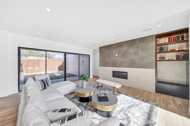 living room featuring visible vents, an accent wall, recessed lighting, a fireplace, and wood finished floors