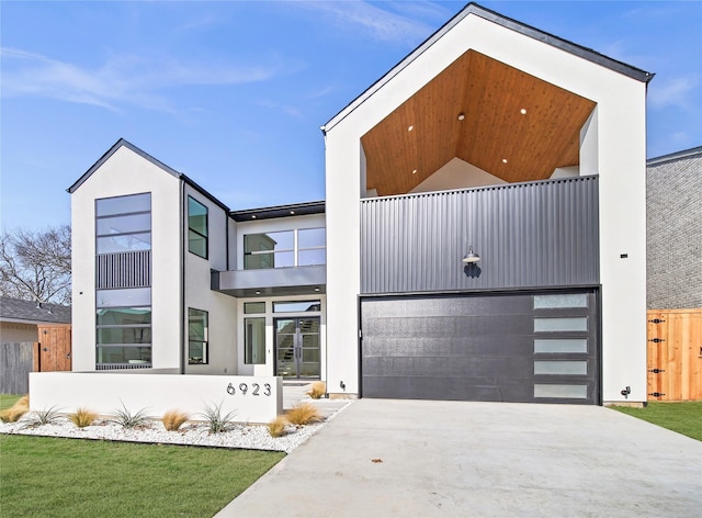 contemporary home with a garage, stucco siding, concrete driveway, and a balcony