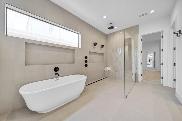 bathroom with visible vents, a freestanding bath, a walk in shower, tile walls, and tile patterned floors