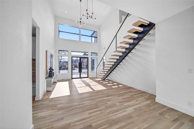 foyer entrance featuring a towering ceiling, light hardwood / wood-style floors, french doors, and a chandelier