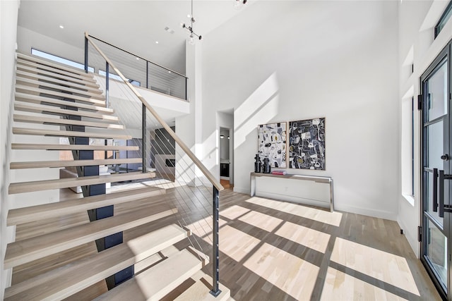 foyer entrance featuring stairway, wood finished floors, baseboards, an inviting chandelier, and a high ceiling