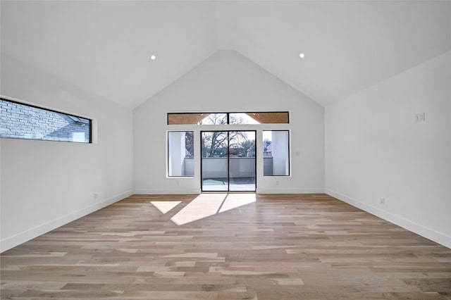 empty room with baseboards, high vaulted ceiling, and light wood finished floors