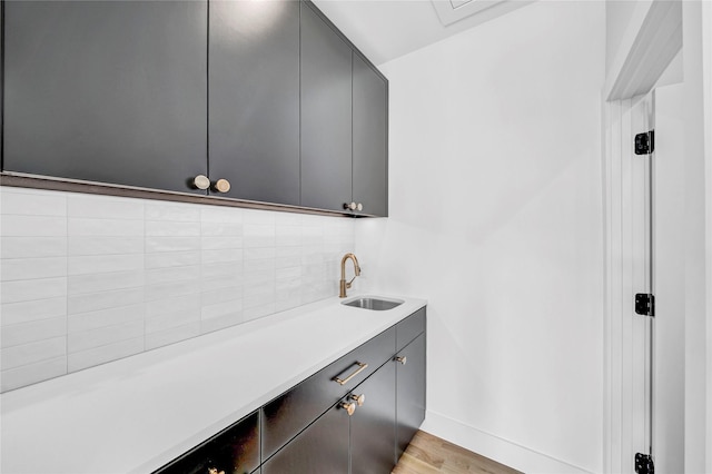 bar with light hardwood / wood-style flooring, sink, decorative backsplash, and gray cabinetry