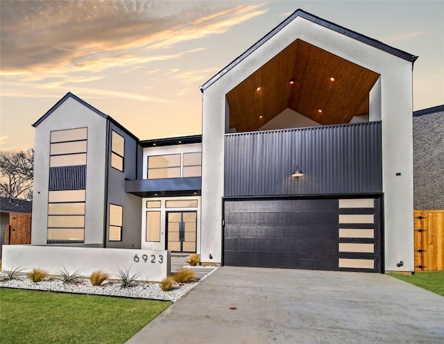 modern home with a balcony, stucco siding, concrete driveway, and a garage