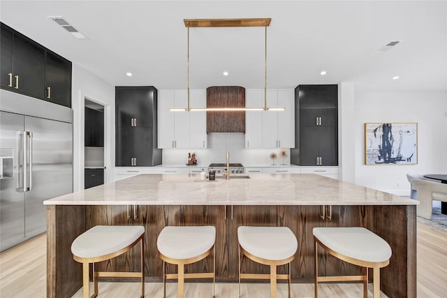 kitchen featuring pendant lighting, stainless steel built in refrigerator, sink, and a center island with sink