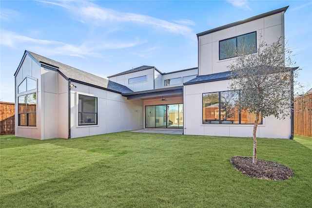 rear view of house featuring a yard, fence, and stucco siding