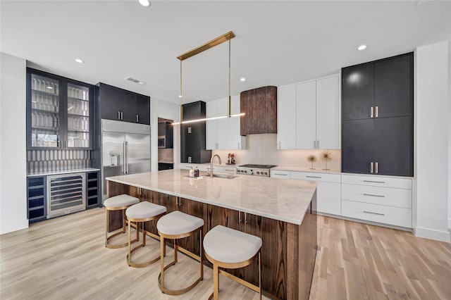 kitchen featuring tasteful backsplash, wine cooler, built in fridge, light wood-style flooring, and a sink