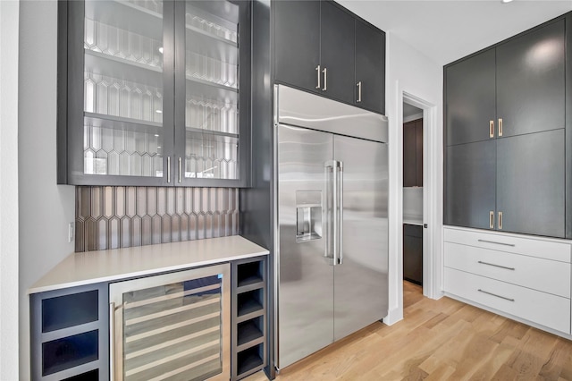 kitchen with light wood-type flooring, built in refrigerator, beverage cooler, dark cabinetry, and glass insert cabinets