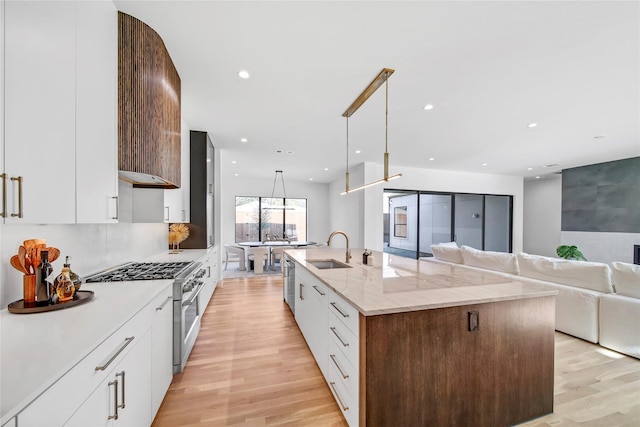 kitchen featuring sink, white cabinets, hanging light fixtures, stainless steel appliances, and a center island with sink