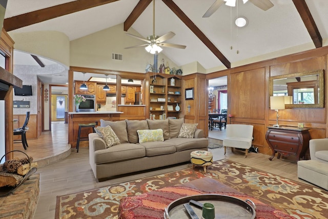 living room with high vaulted ceiling, wooden walls, ceiling fan, beam ceiling, and light hardwood / wood-style floors