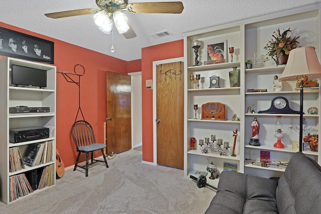 living area with ceiling fan, light carpet, and a textured ceiling