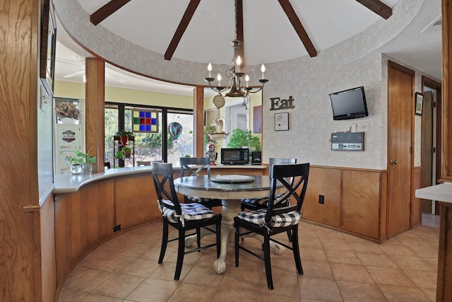 dining space featuring light tile patterned flooring, vaulted ceiling with beams, a chandelier, and wood walls