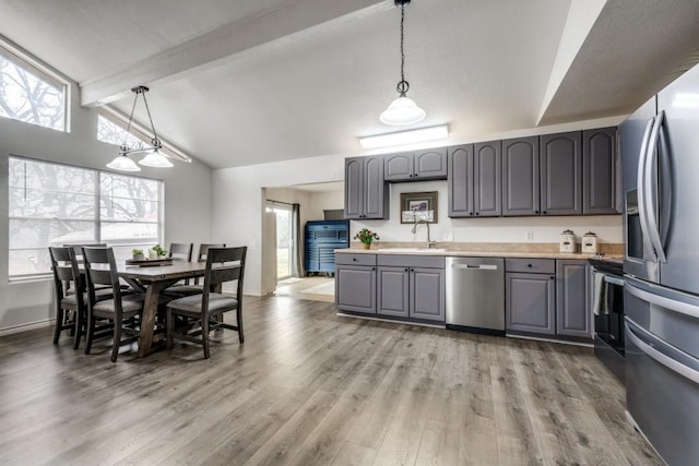 kitchen with vaulted ceiling with beams, gray cabinets, hanging light fixtures, appliances with stainless steel finishes, and a sink