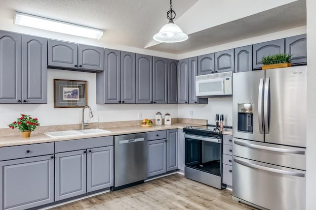 kitchen featuring appliances with stainless steel finishes, light countertops, light wood-type flooring, pendant lighting, and a sink