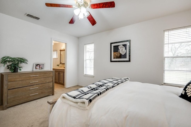 bedroom featuring a ceiling fan, light colored carpet, visible vents, and ensuite bathroom