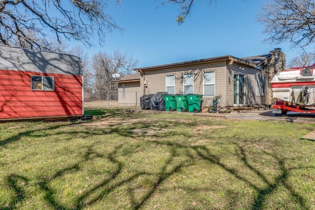 rear view of house with fence, an outdoor structure, and a lawn