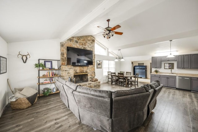 living room featuring vaulted ceiling with beams, ceiling fan, dark wood finished floors, and a stone fireplace