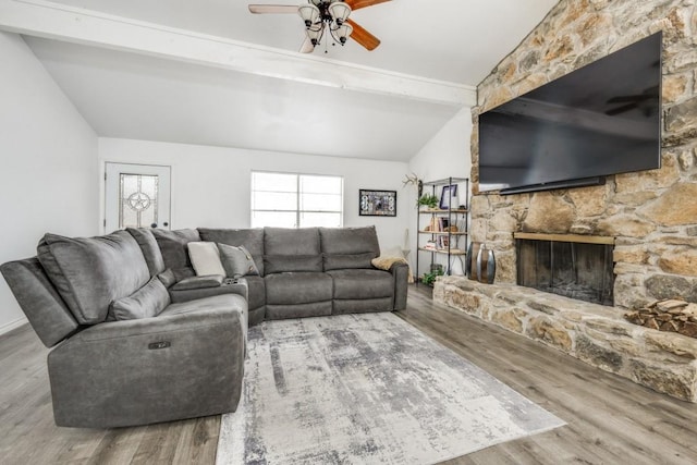 living room featuring a stone fireplace, ceiling fan, lofted ceiling with beams, and wood finished floors