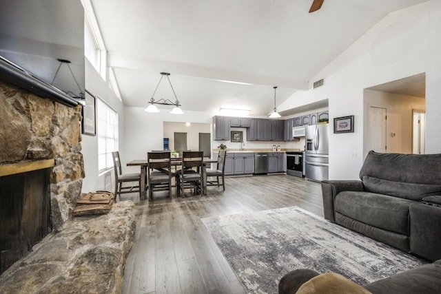 living room with high vaulted ceiling, visible vents, dark wood-type flooring, and a stone fireplace