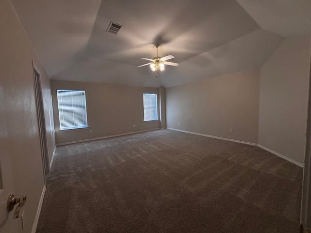 spare room with lofted ceiling, dark colored carpet, visible vents, and baseboards