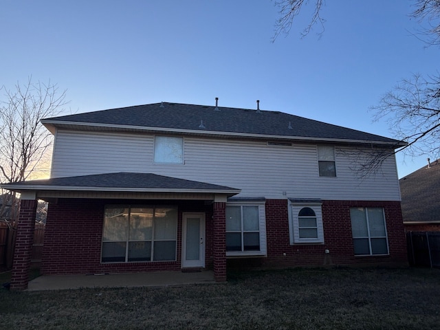 rear view of house with brick siding, a lawn, and roof with shingles