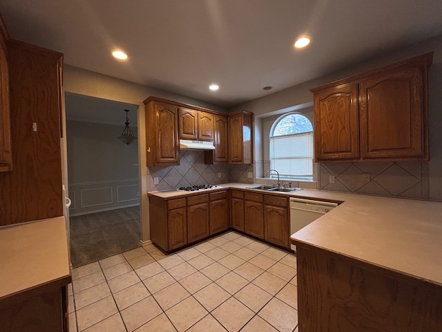 kitchen featuring white dishwasher, light countertops, under cabinet range hood, pendant lighting, and a sink