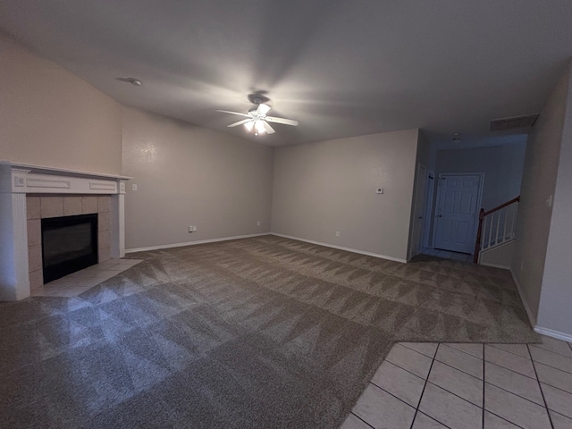 unfurnished living room with ceiling fan, light carpet, visible vents, stairway, and a tiled fireplace