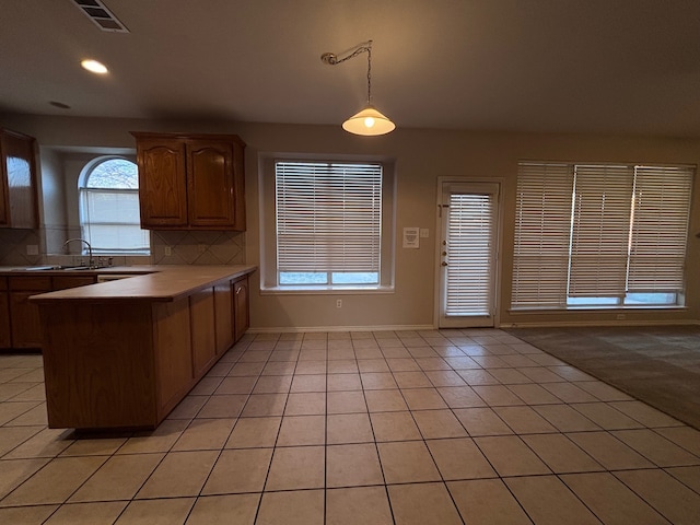 kitchen with tasteful backsplash, visible vents, a peninsula, light countertops, and pendant lighting