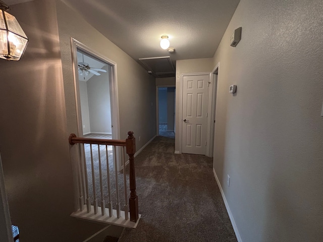 hallway featuring a textured ceiling, dark carpet, an upstairs landing, and baseboards