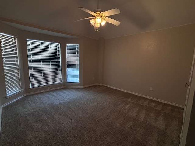 empty room featuring ceiling fan, dark carpet, and baseboards