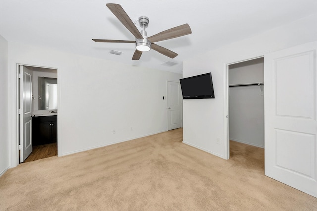 unfurnished bedroom with connected bathroom, a spacious closet, light colored carpet, a closet, and ceiling fan