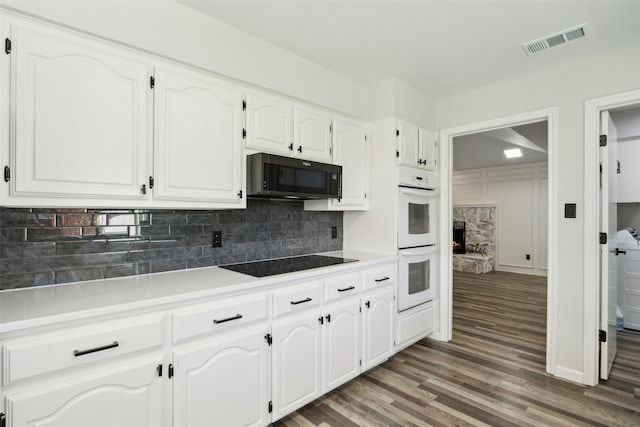 kitchen featuring white cabinetry, a stone fireplace, dark wood-type flooring, and black appliances