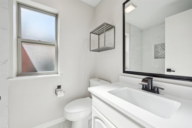 bathroom with vanity, toilet, a healthy amount of sunlight, and tiled shower