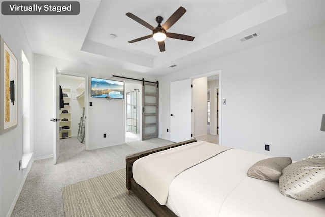 bedroom featuring a raised ceiling, a barn door, light carpet, and ceiling fan