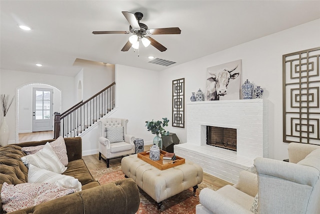 living room featuring a brick fireplace, ceiling fan, and light wood-type flooring