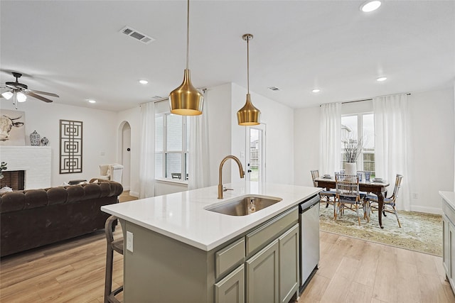 kitchen featuring gray cabinets, pendant lighting, an island with sink, sink, and a brick fireplace