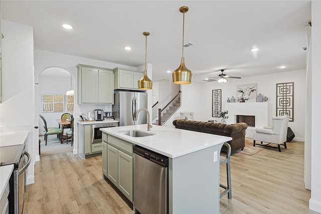 kitchen featuring sink, hanging light fixtures, a kitchen island with sink, stainless steel appliances, and light wood-type flooring