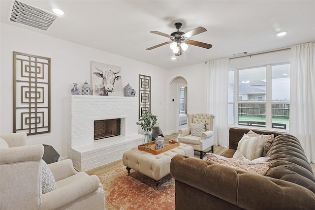 living room featuring wood-type flooring, a brick fireplace, and ceiling fan