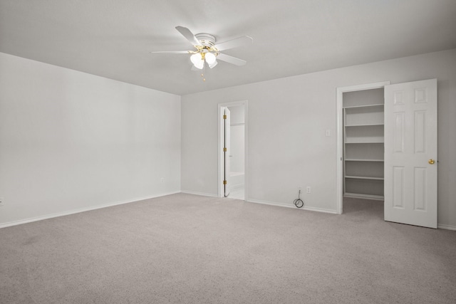 interior space with connected bathroom, a walk in closet, ceiling fan, light carpet, and a closet